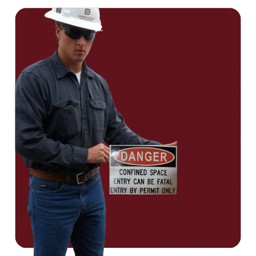 Worker holding a danger sign stating confined space entry can be fatal. Entry by permit only.